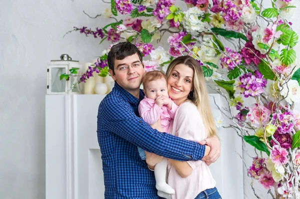 Familia feliz de tres stand en habitación blanca con flores . — Foto de Stock