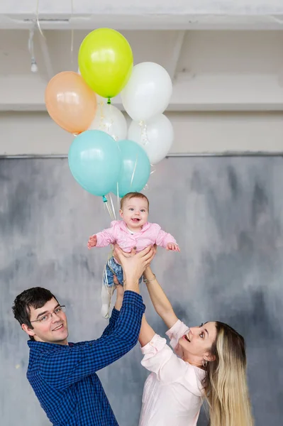 Portrait of a young family with balloons indoors.