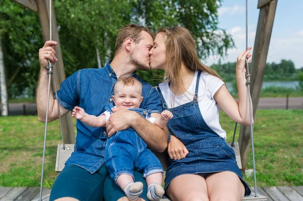 Happy family with baby son on a swing at the playground. — Stock Photo, Image