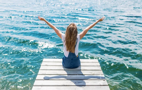 Niedliche fröhliche Teenager-Mädchen sitzt auf einem kleinen Dock und schaut auf den Fluss. — Stockfoto