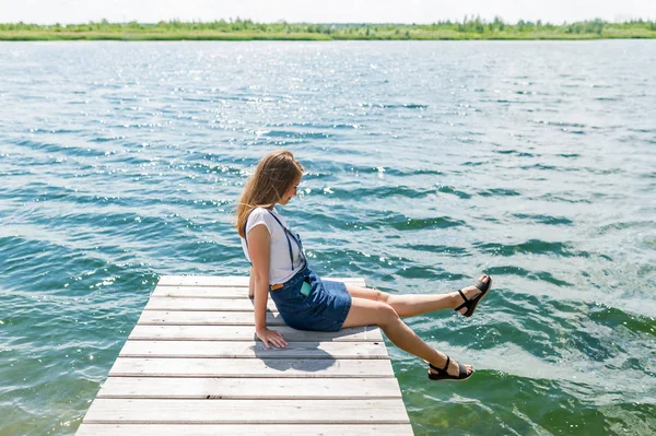 Młoda piękna dziewczyna siedzi na nabrzeży rzeki na tle — Zdjęcie stockowe