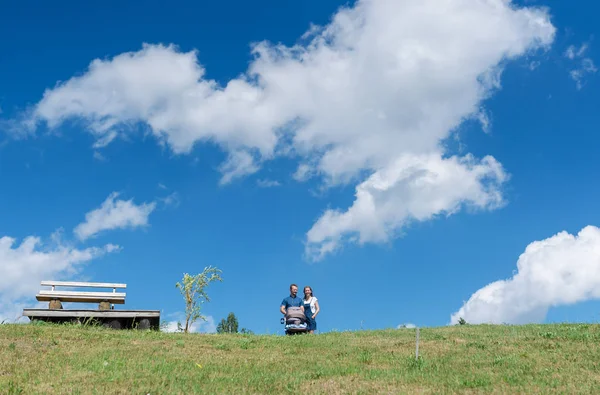 Lycklig familj med bebis på fältet. Grönt fält under blå himmel. Sommarlandskap — Stockfoto