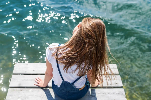 Молодая красивая девушка сидит на пристани реки на заднем плане — стоковое фото