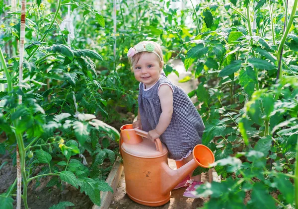 Bebê menina rega uma planta em estufa — Fotografia de Stock