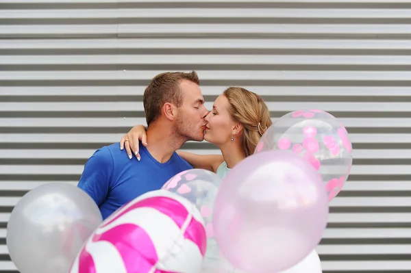 Jeune couple attrayant en amour baisers sur fond rayé et ballons colorés — Photo