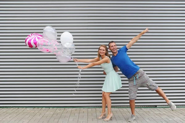 Funky ungt par som holder ballonger mens de hopper mot stripete bakgrunn – stockfoto