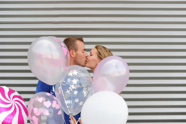 Jeune couple attrayant en amour baisers sur fond rayé et ballons colorés — Photo