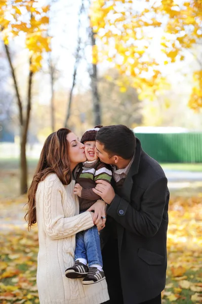 Parents kissing their little son. Portrait of happy caucasian family in autumn park. — Stock Photo, Image