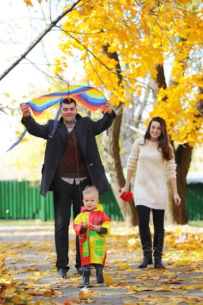 Padre, madre e hijo lindo caminando en el parque amarillo de otoño bajo un paraguas — Foto de Stock