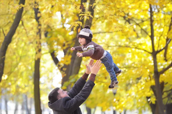 El padre cuida al hijo en el parque de otoño sobre el fondo de una rama de ceniza de montaña — Foto de Stock