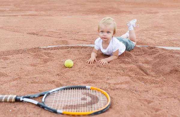 Tenis kortunda yalan küçük kız. Küçük kız, tenis top ve raket
