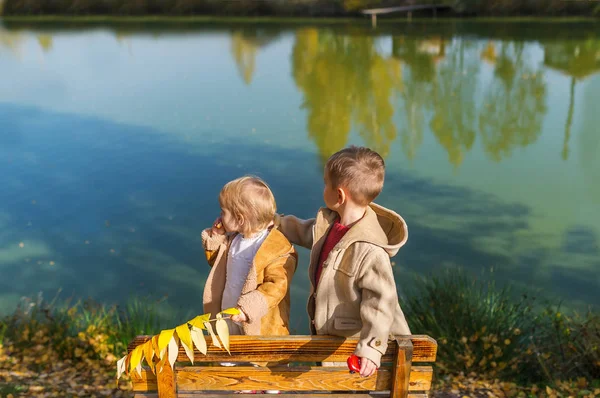 Słodkie dzieci dwa na ławce na zewnątrz z widokiem na jezioro jesień w słoneczny dzień — Zdjęcie stockowe