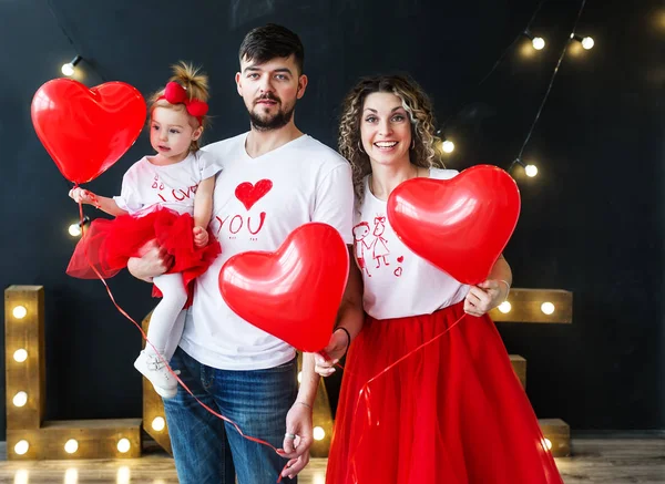 Schöne junge Familie und ihre kleine Tochter posieren mit Luftballons in einem gemütlichen Studio. — Stockfoto