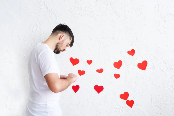 Der junge Mann klebt Valentinstagskarten an eine weiße Wand — Stockfoto