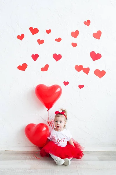 Süßes kleines Mädchen mit rotem Herzen. glückliches kleines Mädchen mit rotem Luftballon an einer leeren Ziegelwand. — Stockfoto