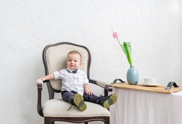 Cute baby boy under 1 year old wearing stylish clothes sitting in vintage chair in home room. — Stock Photo, Image