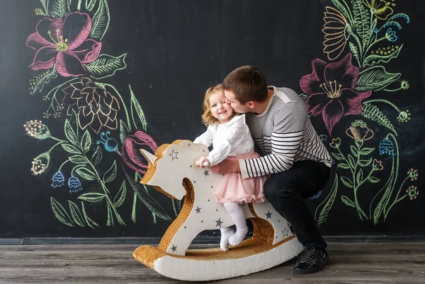 Papá juega con su hija. Padre enrolla a una pequeña hija en un caballo de juguete . — Foto de Stock