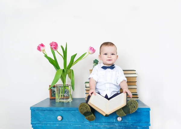 Portrait of the cute small boy sitting on a table with the book in hands — Stock Photo, Image