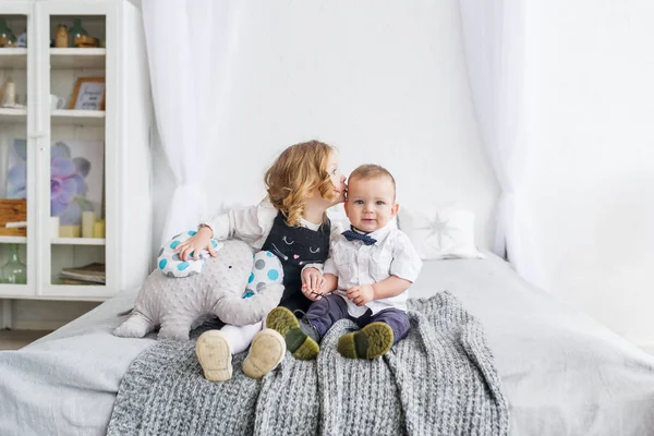 The little sister kisses the brother, staying at home on a bed in the light bedroom — Stock Photo, Image