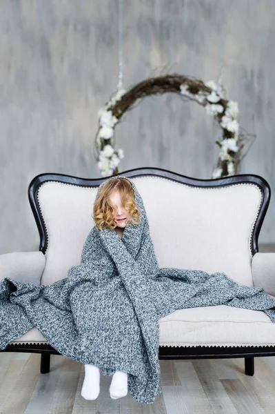 Nettes kleines Mädchen sitzt unter grauer Decke im Sessel zu Hause — Stockfoto