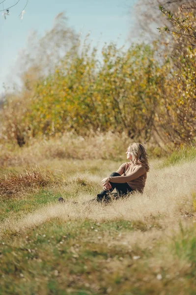 La muchacha descansa sobre la hierba, se sienta y mira soñadoramente a la distancia . — Foto de Stock