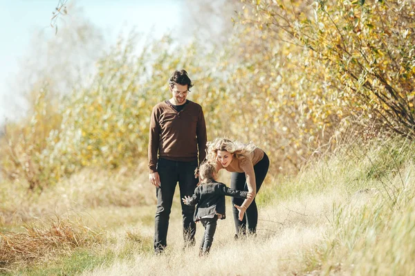Feliz familia joven de tres caminando en la naturaleza de otoño . — Foto de Stock
