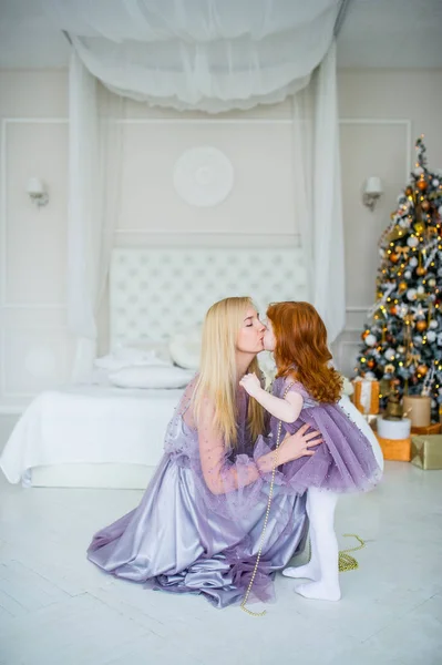 Loira mãe beijando ruiva pequena filha no quarto com decorações na véspera de Natal . — Fotografia de Stock