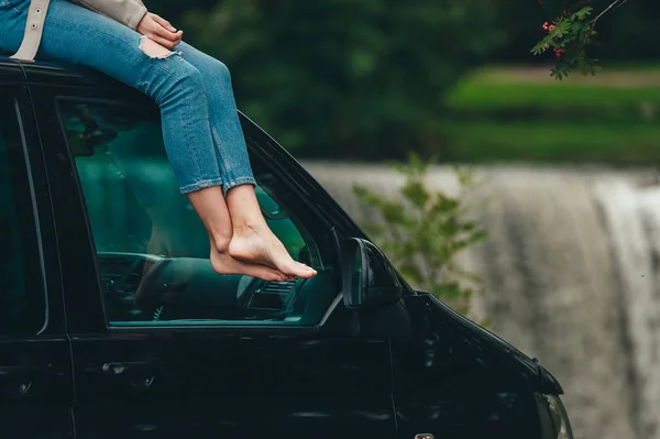 Relaxed lady with bare feet sitting on the roof top of the car.