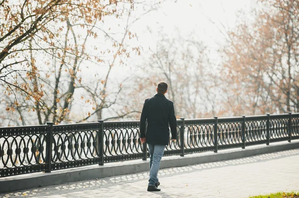 Handsome man in black coat walking around autumn city park. — Stock Photo, Image