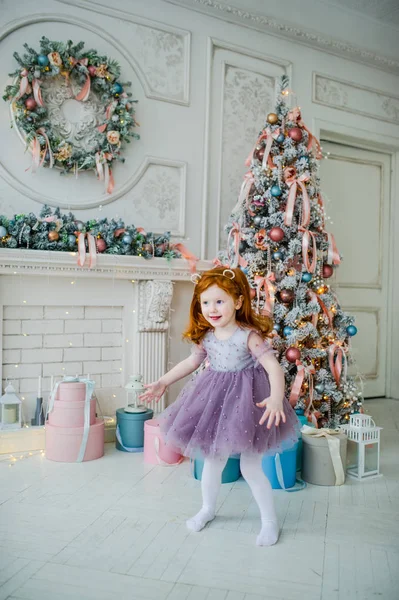 Pequena menina ruiva em um belo vestido dançando perto da árvore de Natal . — Fotografia de Stock