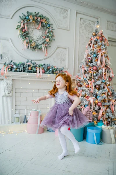 Carino divertente piccola rossa bambino ragazza danza vicino decorato albero di Natale al chiuso — Foto Stock