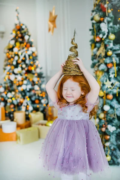 La petite fille aux cheveux roux avec une pyramide d'or sur la tête près du paysage à la mode du Nouvel An — Photo