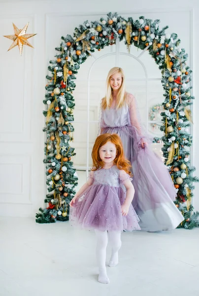 Ruiva filha e sua mãe loira estão tocando antes de arco de ramos de abeto em um estúdio de Natal — Fotografia de Stock