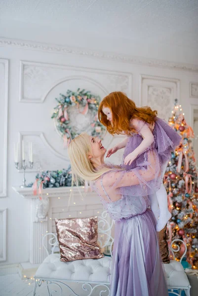 Mother throws up little redhead girl in the decorated room with Christmas tree. — Stock Photo, Image