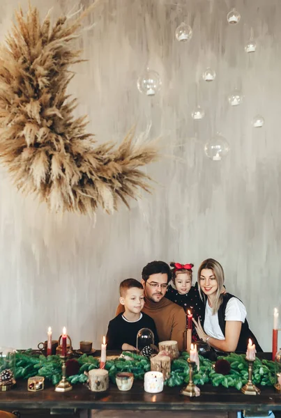 Joven familia feliz de cuatro cerca de la mesa de Navidad con ramas de abeto y velas . — Foto de Stock