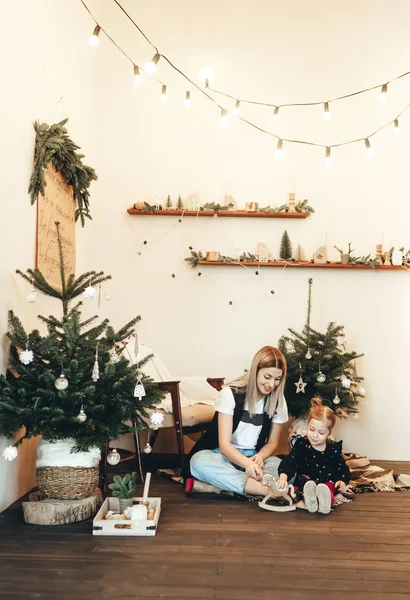 Mother and her little daughter sitting and playing on a floor next to a Christmas tree at home — Stock Photo, Image