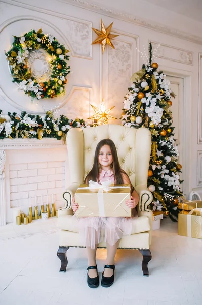 Menina em vestido rosa sentado na poltrona pela árvore de Natal no quarto do Ano Novo . — Fotografia de Stock