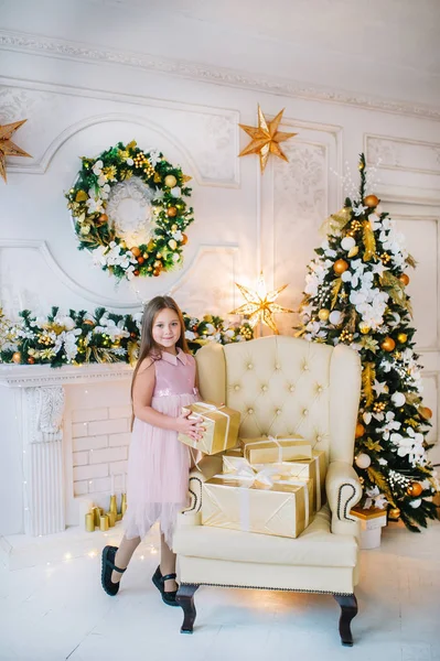 Bambina in abito rosa è in piedi sulla poltrona vicino all'albero di Natale nella stanza del nuovo anno . — Foto Stock