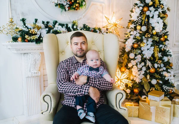Glücklicher entzückender Vater mit Kind sitzt neben geschmücktem Neujahrsbaum. — Stockfoto