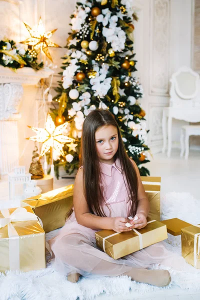Menina sentada no chão perto da árvore de natal, segurando caixa de presente de ouro — Fotografia de Stock