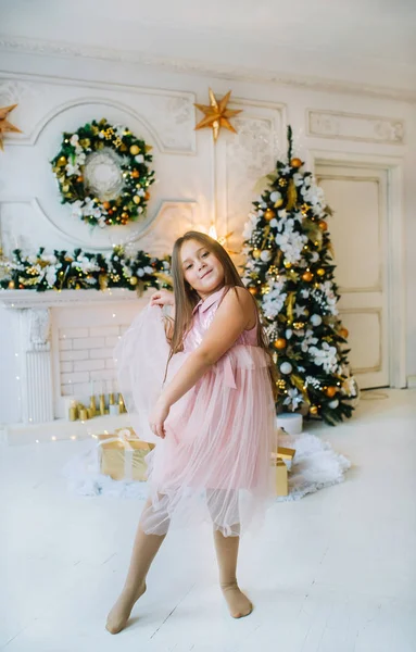 Joven hermosa chica en vestido rosa está bailando en habitación blanca cerca del árbol de Navidad — Foto de Stock