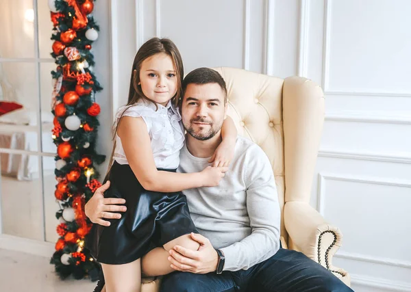 Feliz padre con hija sentada en un sillón cerca del árbol de Navidad . — Foto de Stock