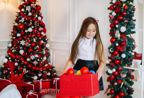 Позитивная маленькая девочка с кошачьими ушами держит коробку со множеством рождественских шаров — стоковое фото