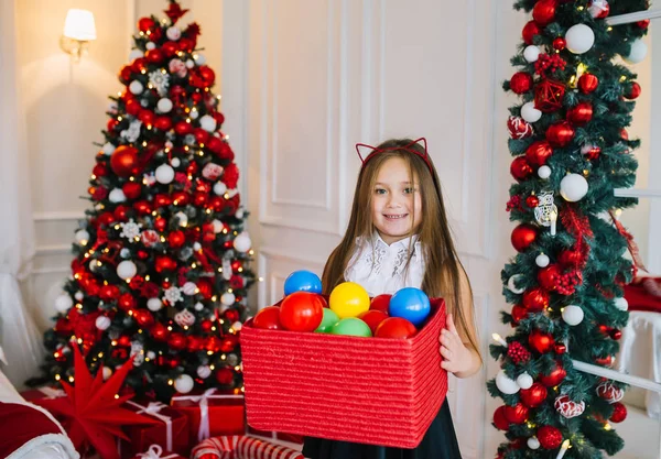 Positivo pouco alegre gato menina segurar caixa com bolas para árvore de Natal dentro de casa . — Fotografia de Stock