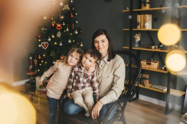 Noel ağacının yanında mutlu anne ve iki çocuğun portresi. Arka planda bir Noel ağacı.