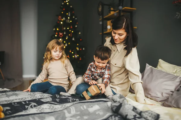 Madre con sus lindos niños pequeños abriendo regalos de Navidad en la cama . —  Fotos de Stock