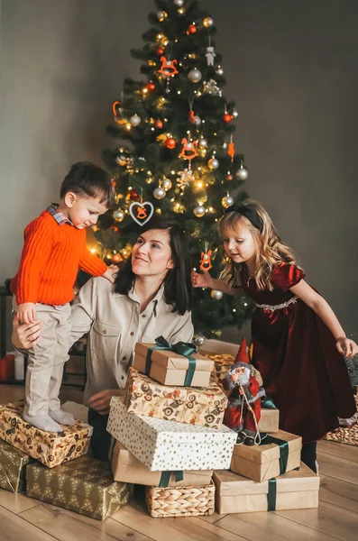 Madre cariñosa regala a sus hijos pequeños cerca de un árbol de Navidad festivo . — Foto de Stock
