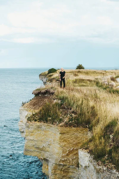 Turystka stojąca na trawie na skraju skalistego wybrzeża Morza Bałtyckiego. — Zdjęcie stockowe