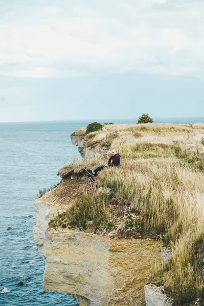 Una pareja sentada en la hierba en el borde de la costa rocosa del mar Báltico . — Foto de Stock