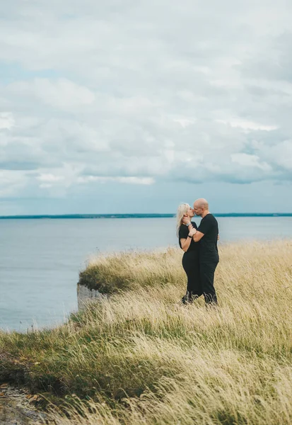 Romantic view of couple in black clothes when they kiss on the edge of the rocky coast of the Baltic sea.